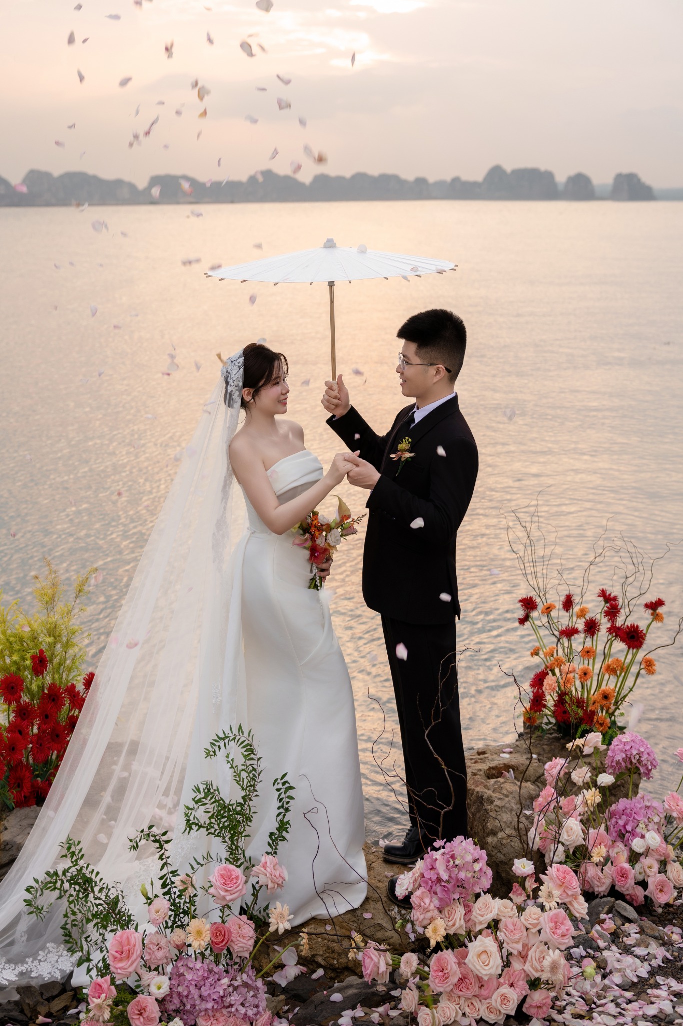 Cô dâu chú rể bên chiếc ô và cánh hoa bay